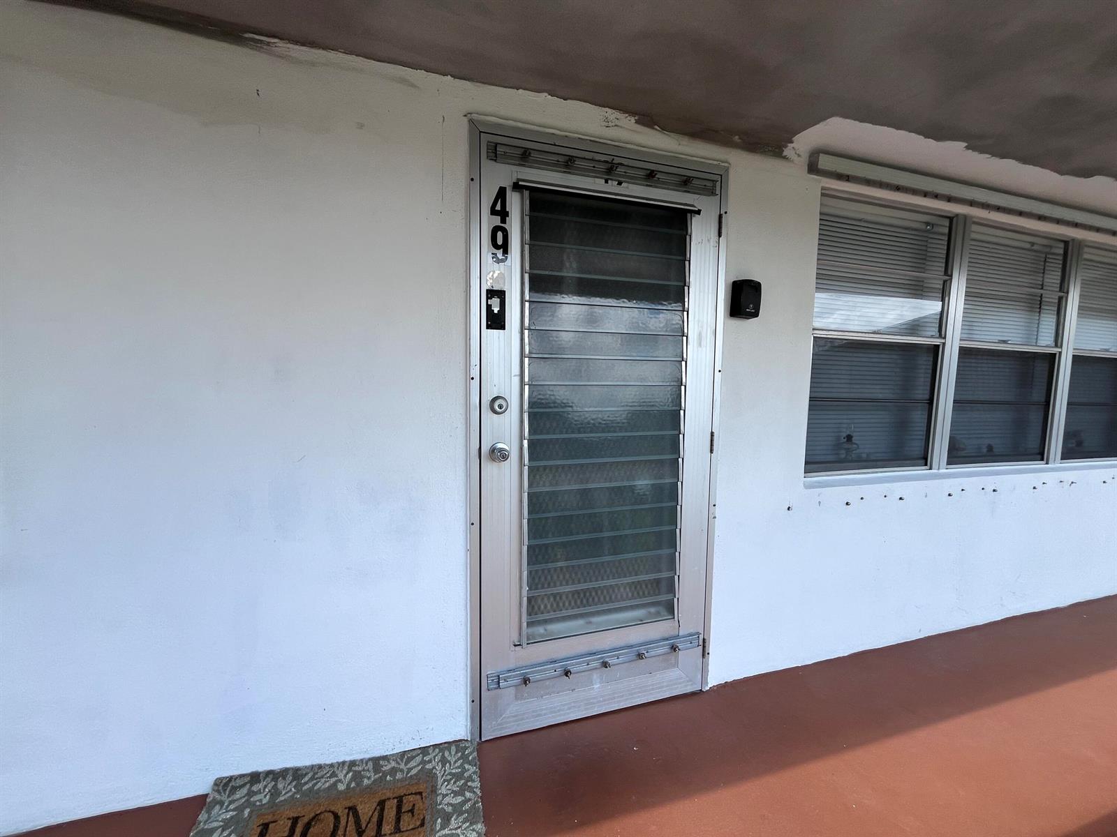 A white exterior wall features a metal door with horizontal glass slats and a window — 49 Cambridge B, West Palm Beach FL 33417, WEST PALM BEACH, FL