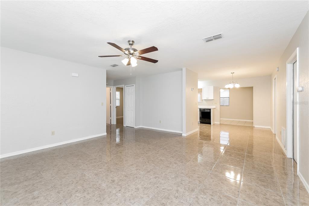 A spacious living area with light-colored tile flooring, a ceiling fan, and an adjacent kitchen — 240 GRIFFORD DRIVE, KISSIMMEE, FL