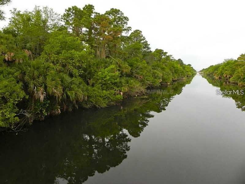 A calm canal flows alongside a dense line of lush green trees and palm plants — Lot#40 INVERNESS STREET, NORTH PORT, FL
