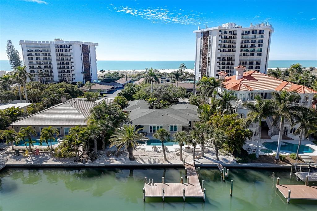An aerial view shows three waterfront houses with pools and docks near two large apartment buildings — 39 S POLK DRIVE, SARASOTA, FL