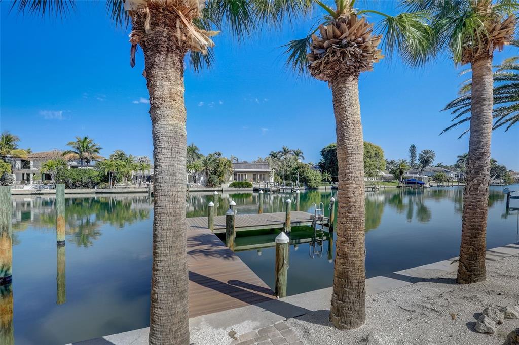 A wooden dock extends into a calm canal framed by palm trees under a clear sky — 39 S POLK DRIVE, SARASOTA, FL