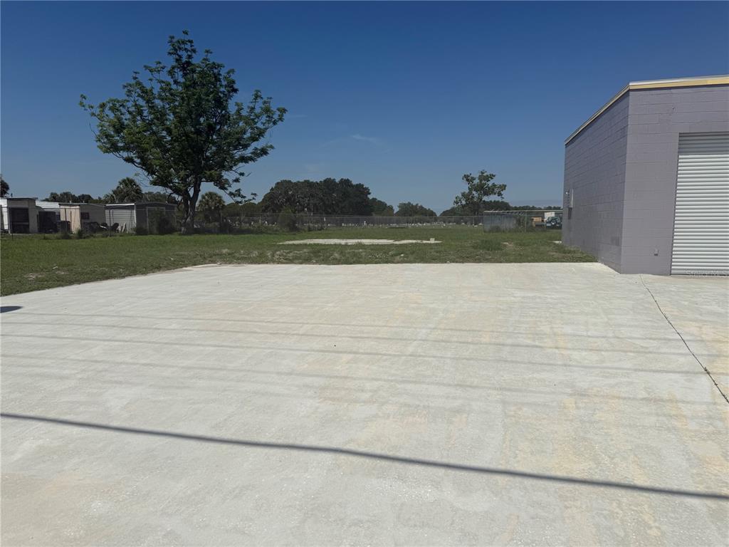 A large concrete parking area sits beside a gray industrial building under a clear sky — 20600 HWY 27, LAKE WALES, FL