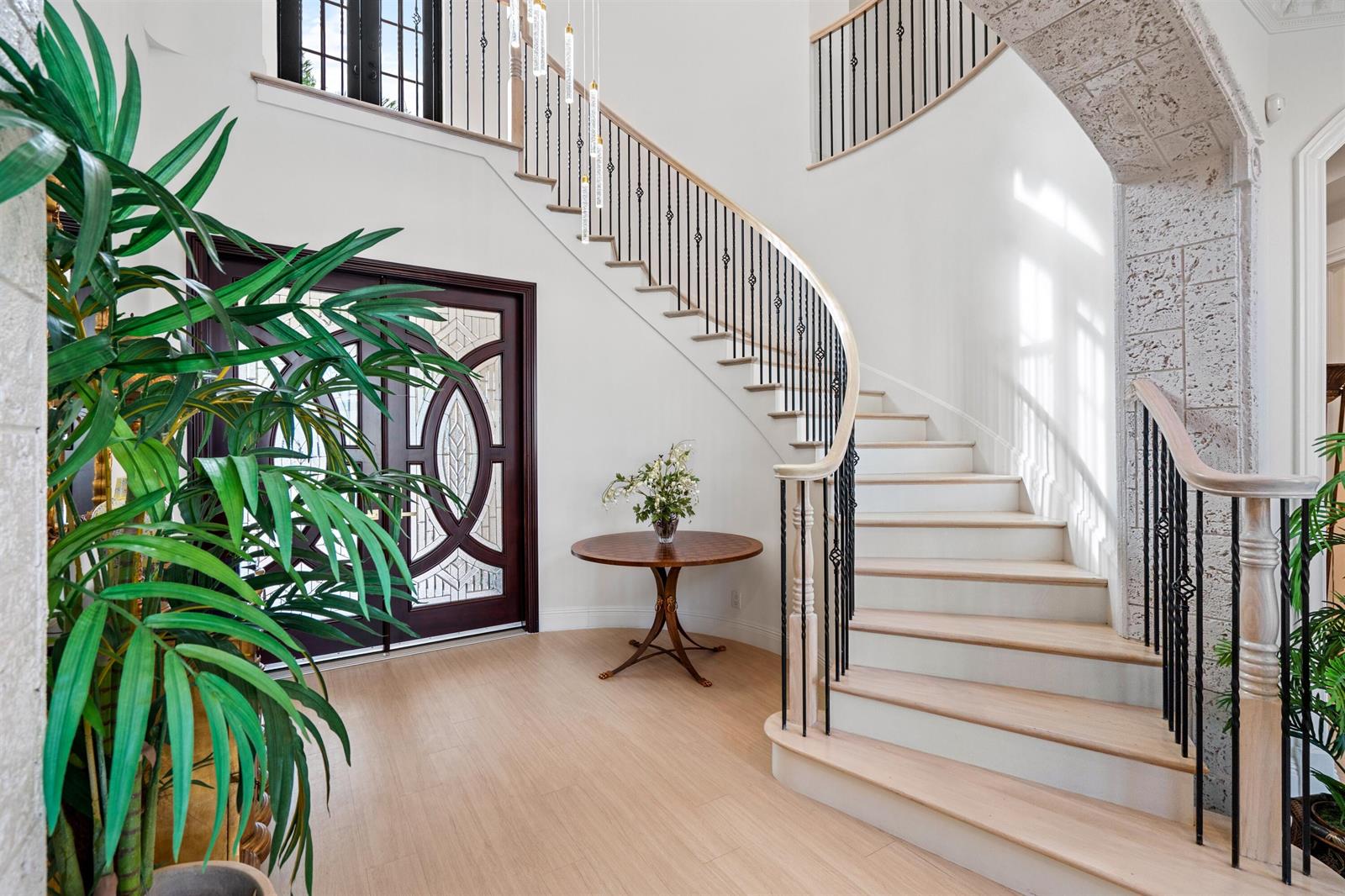A grand foyer features a curved staircase, light wood flooring, and a dark wood front door — 17894 Monte Vista Drive, Boca Raton FL 33496, BOCA RATON, FL