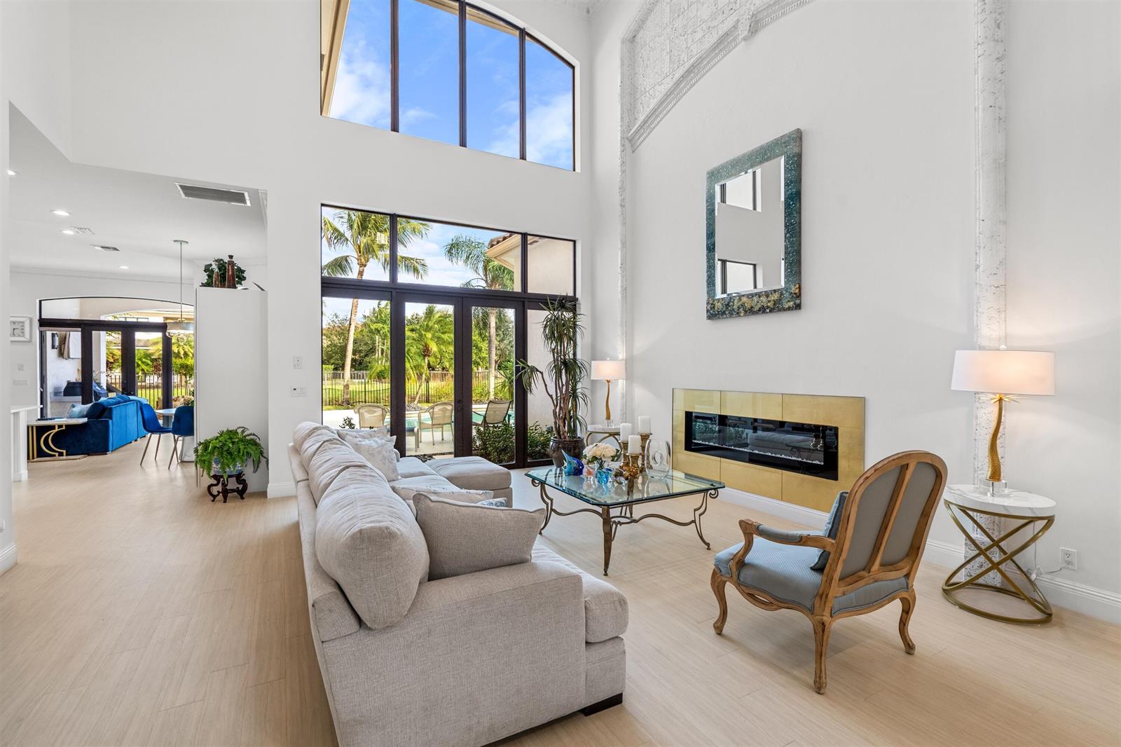 A bright living room features a tall fireplace, floor-to-ceiling windows, and light wood flooring — 17894 Monte Vista Drive, Boca Raton FL 33496, BOCA RATON, FL