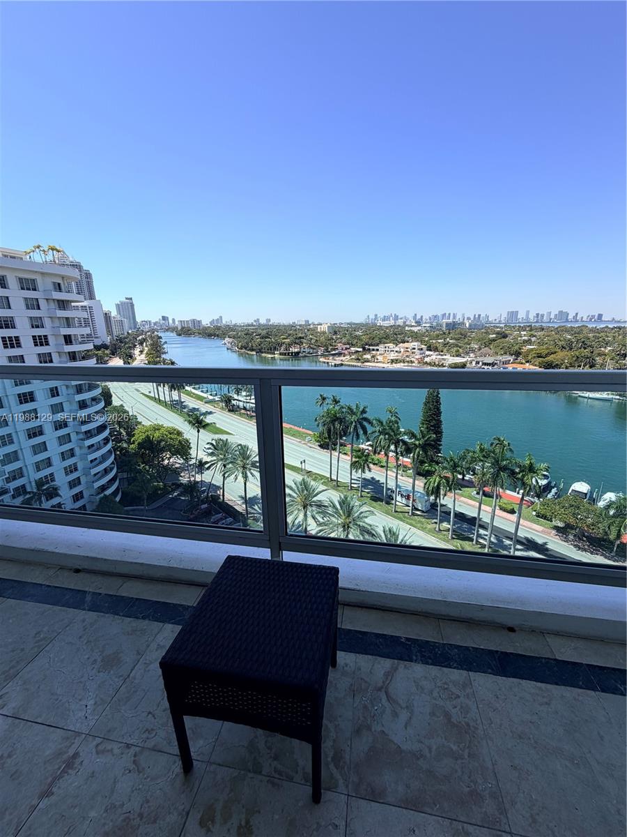 A balcony with a black table overlooks a waterway, a road, and a city skyline — 5161 Collins Ave # 1506, Miami Beach FL 33140, MIAMI BEACH, FL