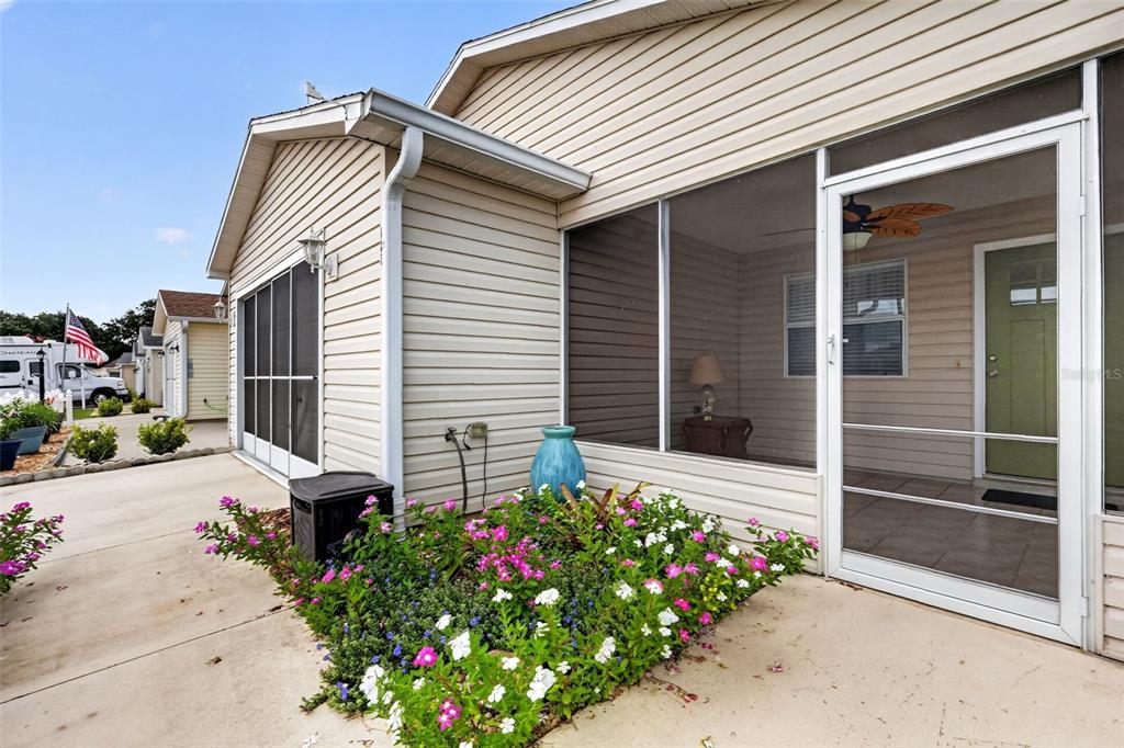 A house exterior features a screened-in porch, a concrete patio, and a small flower garden — 483 HILDALGO DRIVE, THE VILLAGES, FL