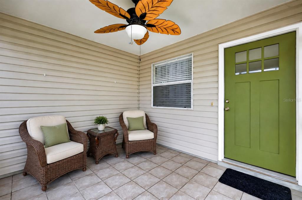 A covered porch features wicker chairs, a small table, and a green front door — 483 HILDALGO DRIVE, THE VILLAGES, FL