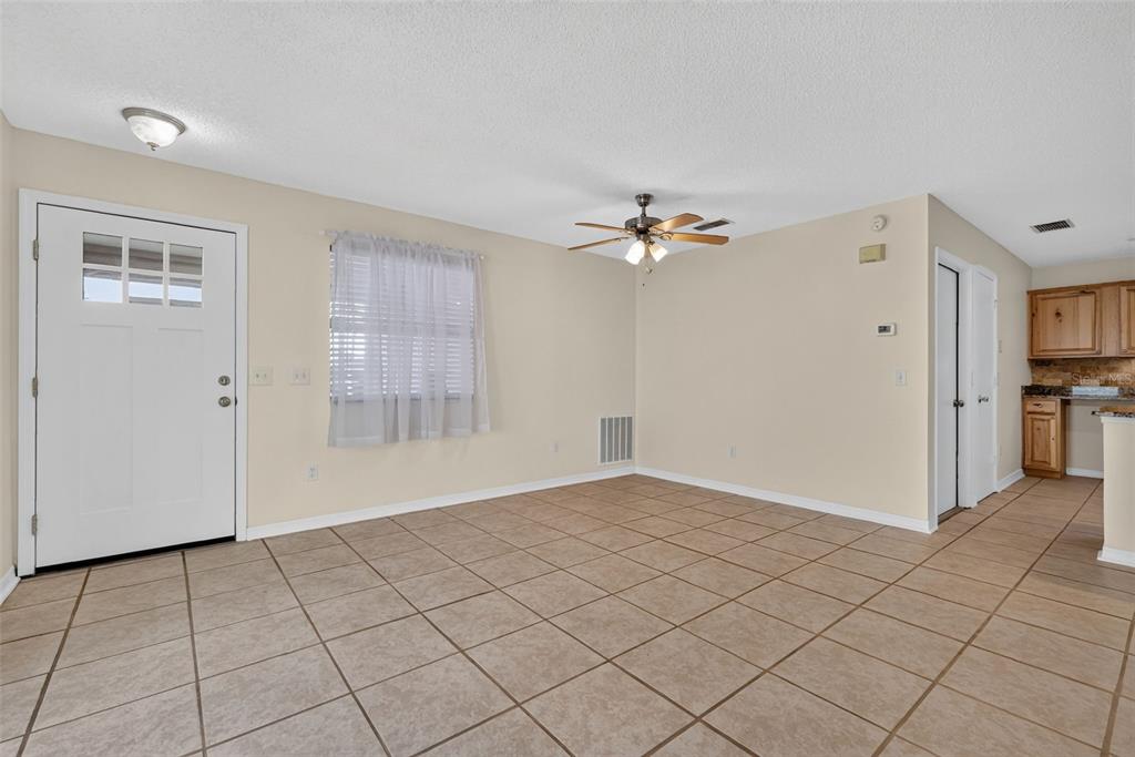 An empty room with beige tile flooring, a ceiling fan, and a white entry door — 483 HILDALGO DRIVE, THE VILLAGES, FL