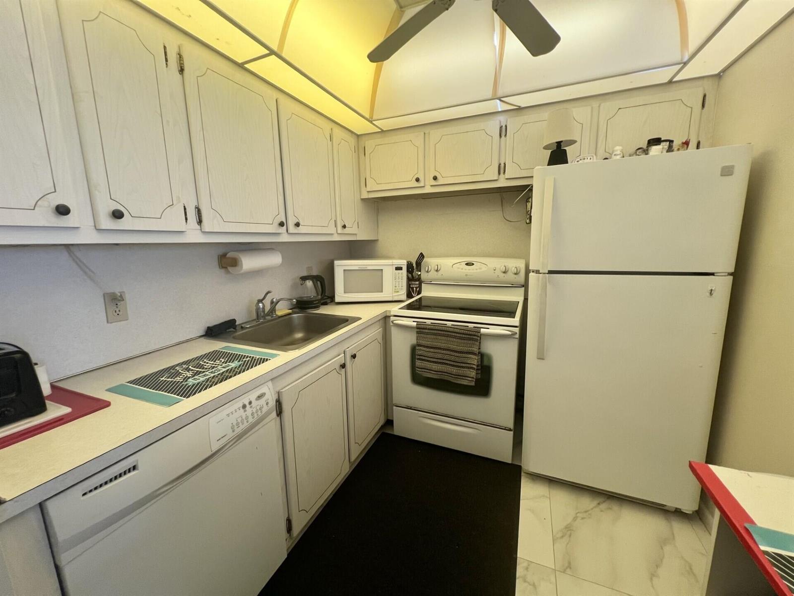 A small kitchen features white cabinets, white appliances, a stainless steel sink, and tile flooring — 3 Islewood A # 3, Deerfield Beach FL 33442, DEERFIELD BEACH, FL