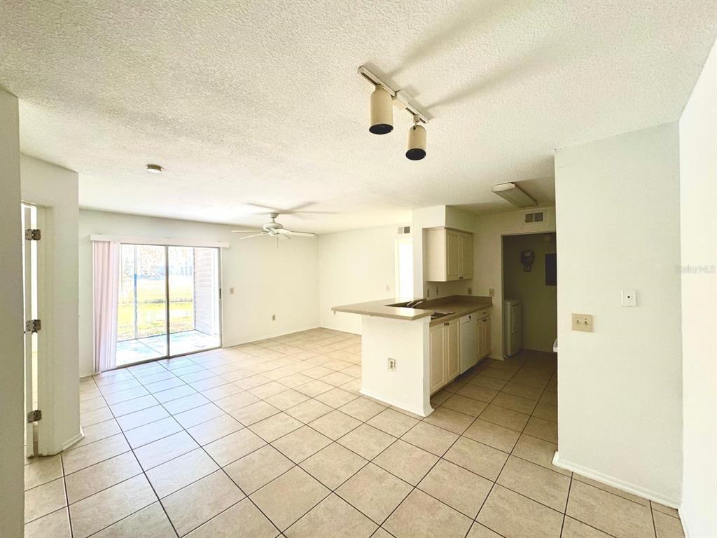 An open-concept living and kitchen area features tile flooring, a breakfast bar, and sliding doors — 1222 BERMUDA LAKES LANE UNIT 106, KISSIMMEE, FL