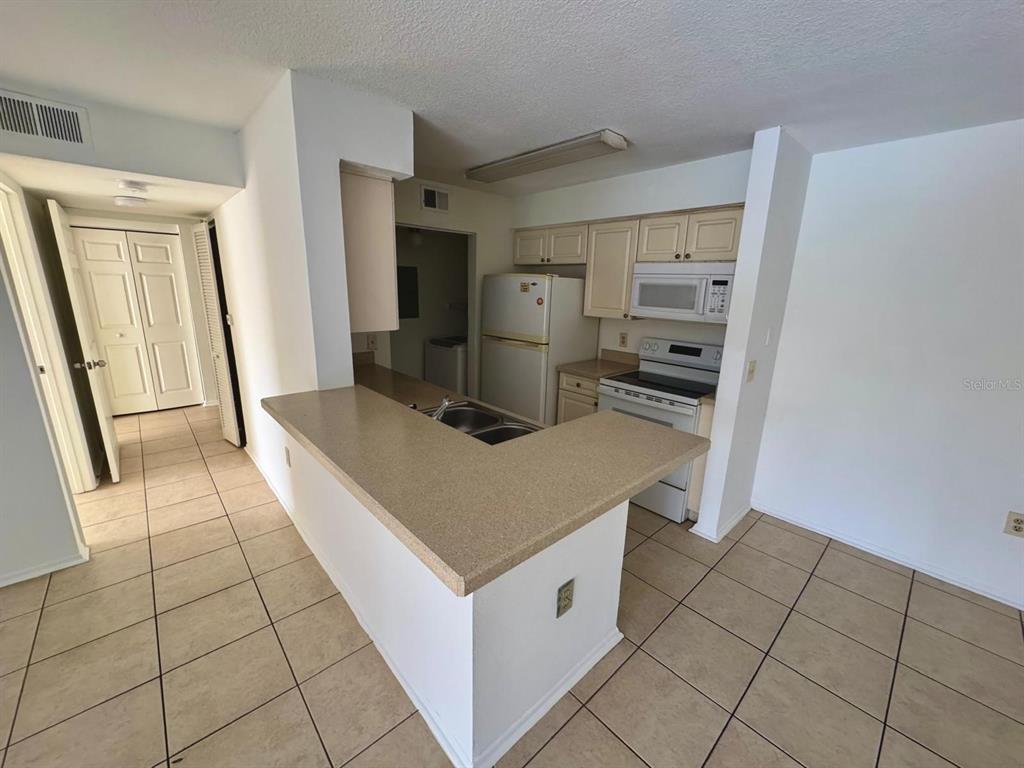 A kitchen with white cabinets, white appliances, and a beige countertop breakfast bar — 1222 BERMUDA LAKES LANE UNIT 106, KISSIMMEE, FL