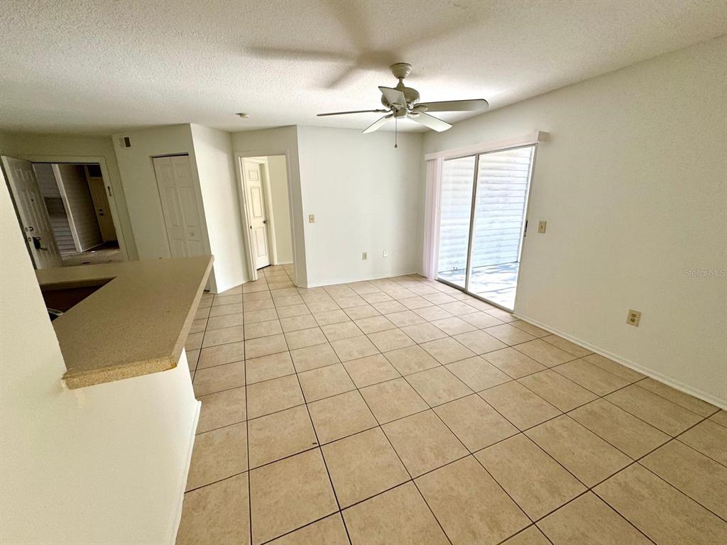 An empty room with beige tile flooring, a ceiling fan, and sliding glass doors — 1222 BERMUDA LAKES LANE UNIT 106, KISSIMMEE, FL