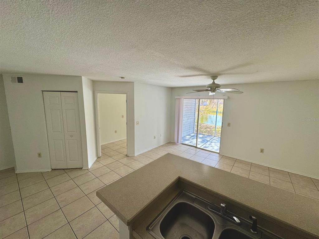 A kitchen island overlooks a living area with tile floors and a sliding glass door — 1222 BERMUDA LAKES LANE UNIT 106, KISSIMMEE, FL