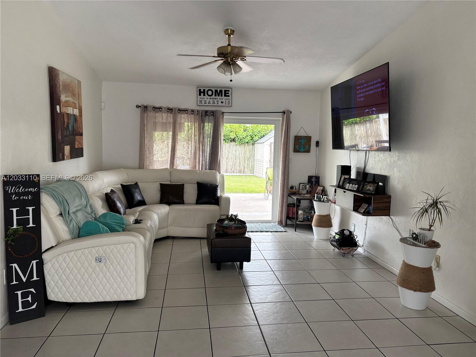 A living room features a white sectional sofa, a wall-mounted television, and a sliding glass door — 11104 SW 155th Ter, Miami FL 33157, MIAMI, FL