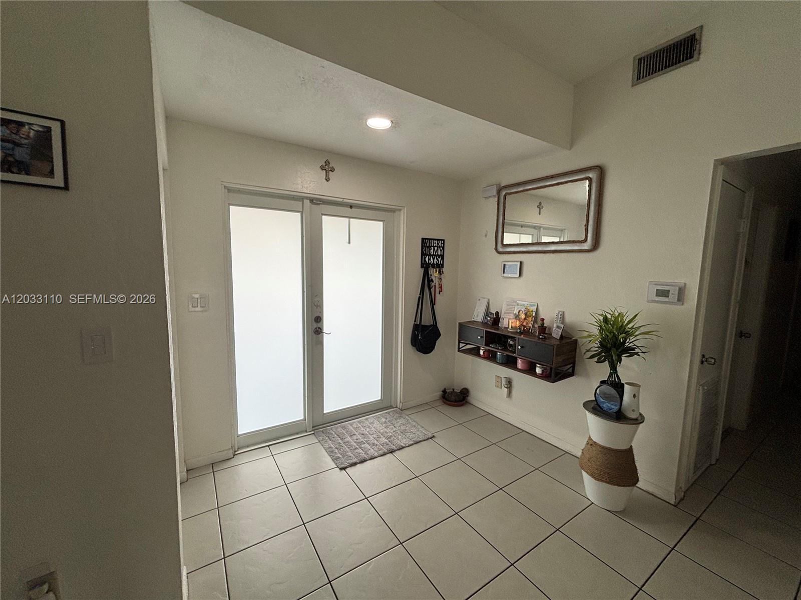 This entryway features white tile flooring, a double glass door, and a wall-mounted storage shelf — 11104 SW 155th Ter, Miami FL 33157, MIAMI, FL