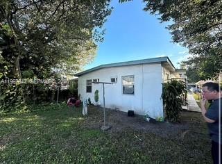 A side view of a white, single-story house with a clothesline in the yard — 1785 NW 56th St, Miami FL 33142, MIAMI, FL