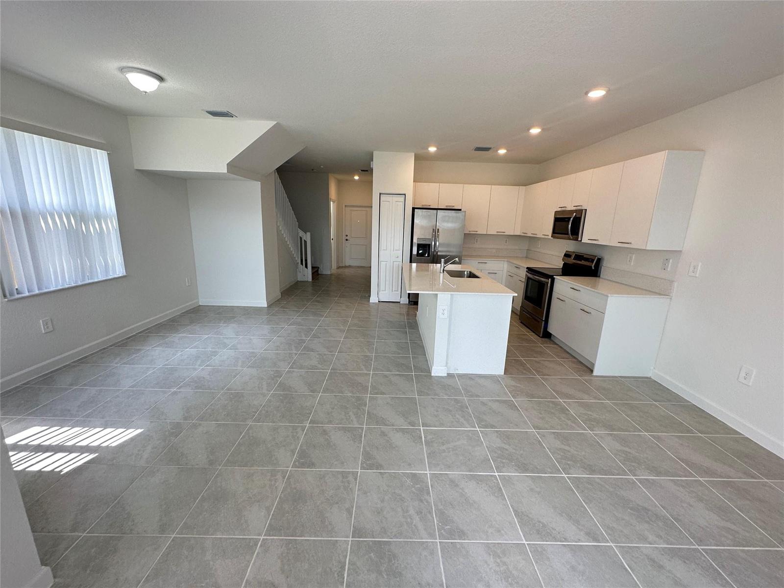 An open-concept kitchen features white cabinetry, a central island, and gray tiled flooring — 2437 NW 131st Circle, Miami FL 33167, MIAMI, FL