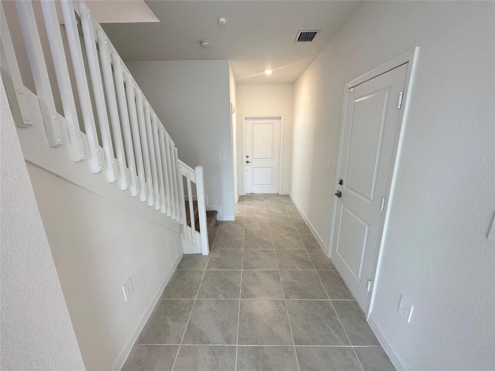 A hallway with gray tile flooring, white walls, a staircase, and two white doors — 2437 NW 131st Circle, Miami FL 33167, MIAMI, FL
