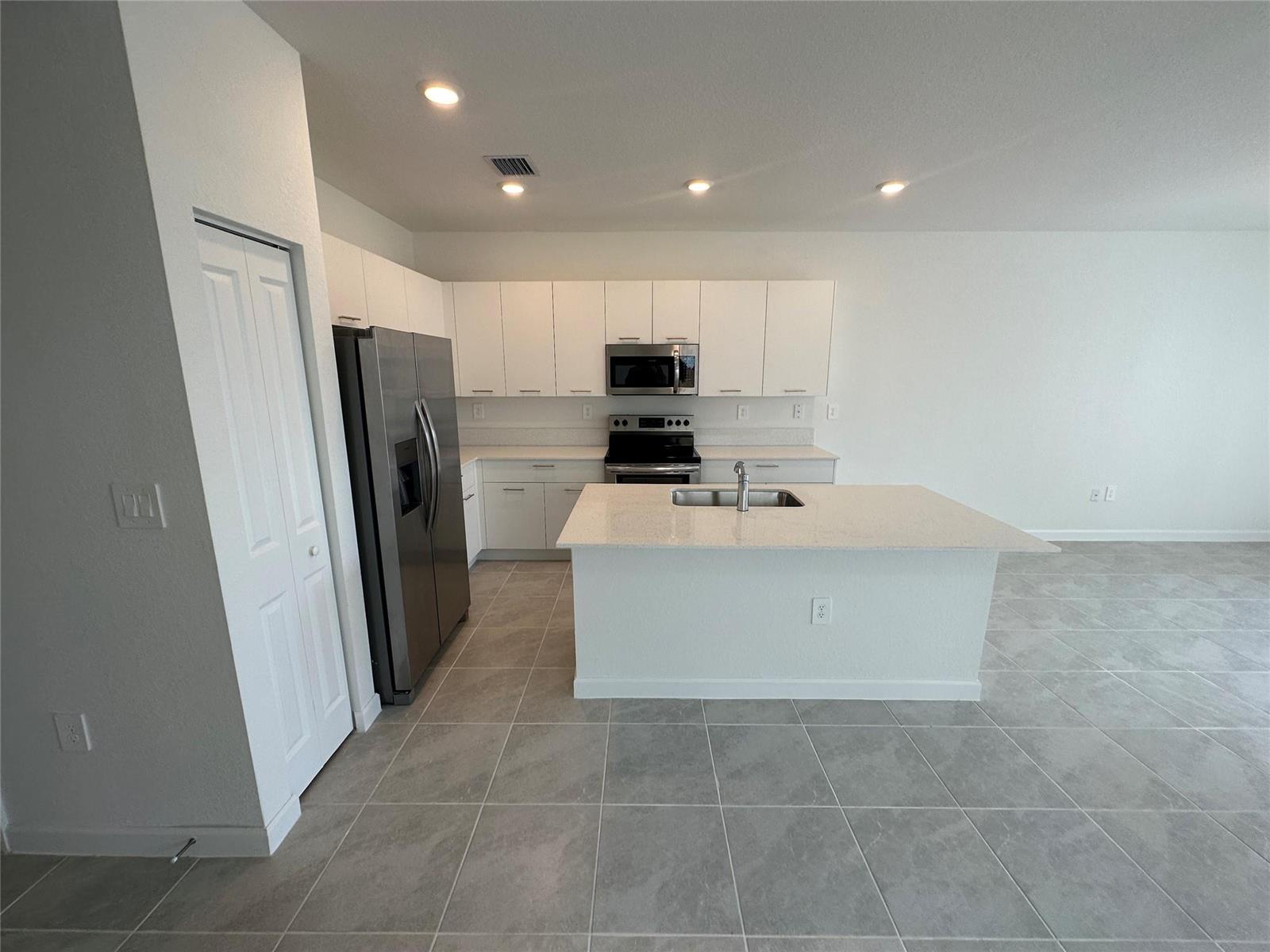 A modern kitchen features white cabinets, stainless steel appliances, a center island, and tiled floors — 2437 NW 131st Circle, Miami FL 33167, MIAMI, FL