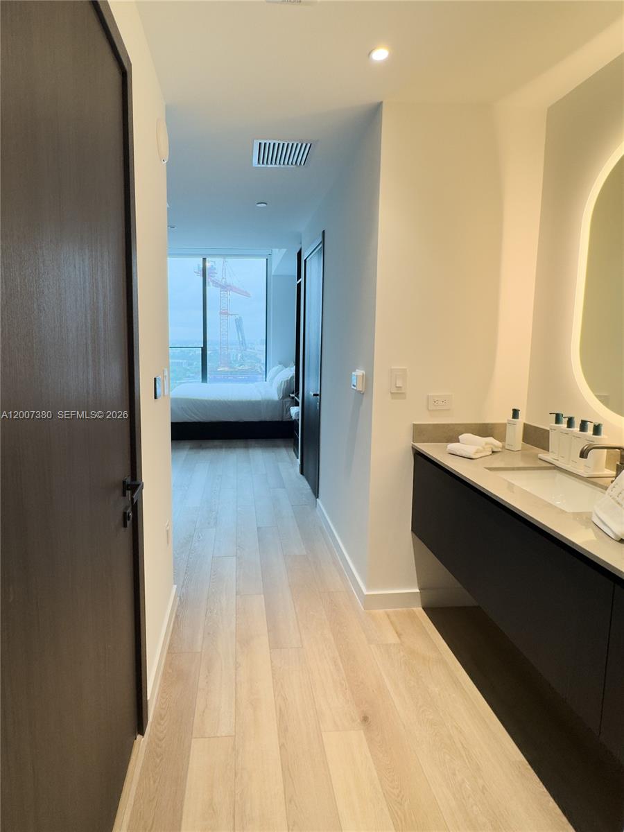 A modern bathroom with a floating vanity leads into a bedroom with floor-to-ceiling windows — 20 NE 11th St # 3012A, Miami FL 33132, MIAMI, FL