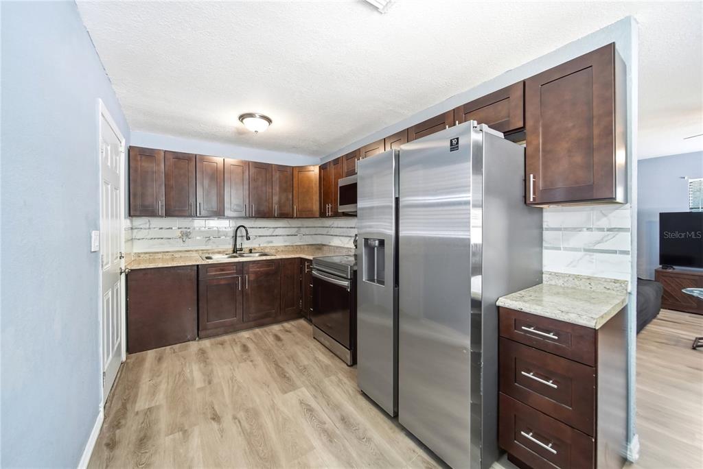 A kitchen features dark wood cabinets, stainless steel appliances, and light-colored granite countertops — 1401 RADLEIGH PLACE, ORLANDO, FL