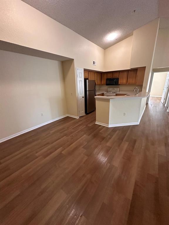 A kitchen with wood cabinets and stainless steel appliances overlooks a living area with flooring — 13013 MULBERRY PARK DRIVE UNIT 224, ORLANDO, FL