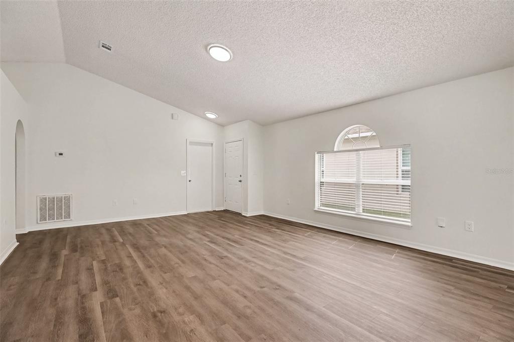 An empty living room features white walls, vaulted ceilings, recessed lighting, and wood-look flooring — 2056 REDWOOD CIRCLE NE, PALM BAY, FL