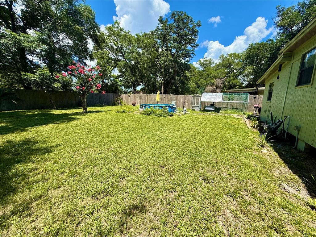 A grassy backyard features a small above-ground pool, a flowering tree, and a wooden fence — 5937 UONA AVENUE, ORLANDO, FL