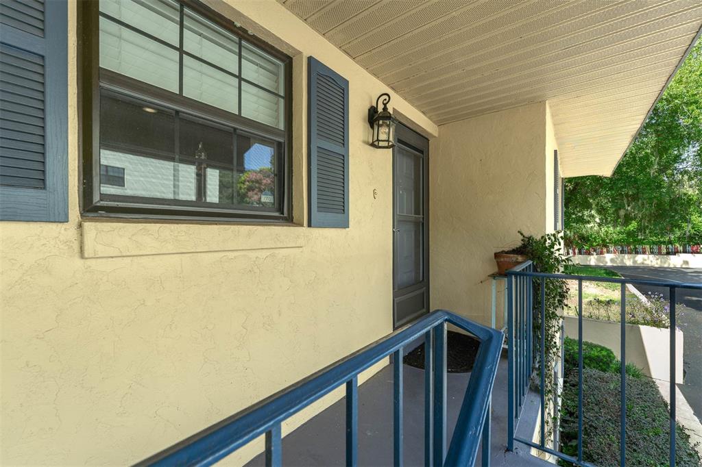 A yellow stucco exterior wall features a window with blue shutters and a front door — 110 N TREMAIN STREET UNIT 209, MOUNT DORA, FL