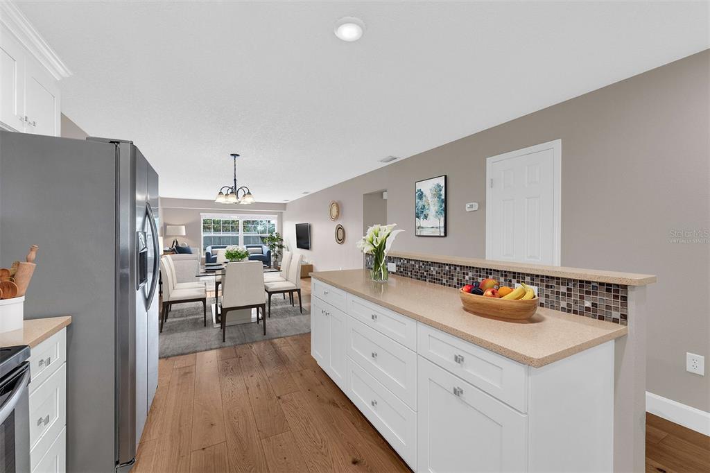 A kitchen island with white cabinets and a tan countertop overlooks a dining area — 110 N TREMAIN STREET UNIT 209, MOUNT DORA, FL