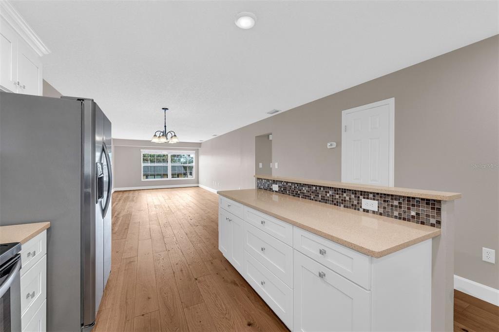 A kitchen with white cabinets and a tiled backsplash overlooks a spacious, open-concept living area — 110 N TREMAIN STREET UNIT 209, MOUNT DORA, FL