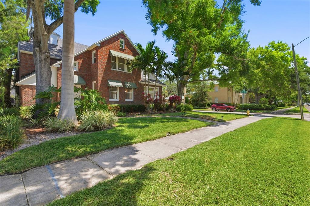 A two-story brick house with green awnings sits on a corner lot with a sidewalk — 555 18TH AVENUE NE, ST PETERSBURG, FL