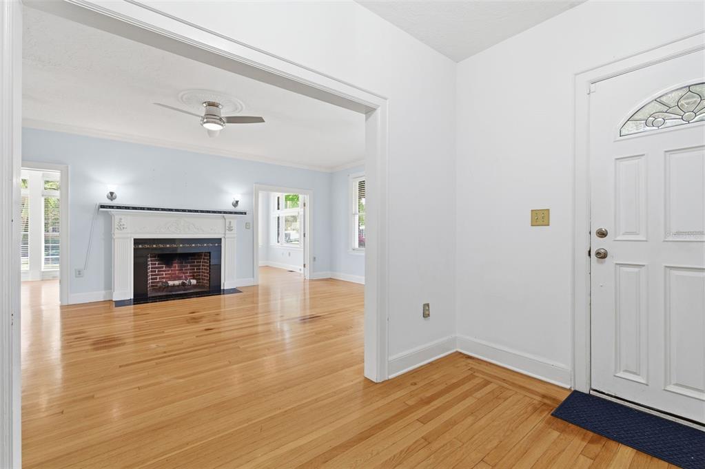 An entryway with hardwood floors leads into a living room featuring a fireplace and ceiling fan — 555 18TH AVENUE NE, ST PETERSBURG, FL