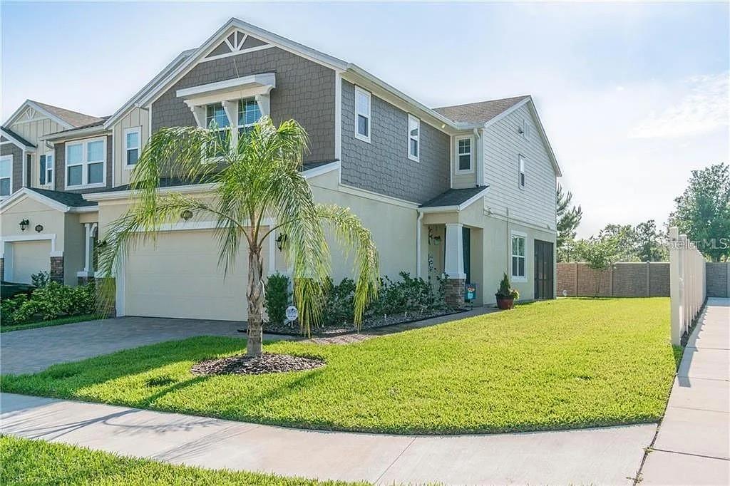 A two-story suburban house features a tan stucco exterior, a brick driveway, and a palm tree — 18814 CORNUTA STREET, LUTZ, FL