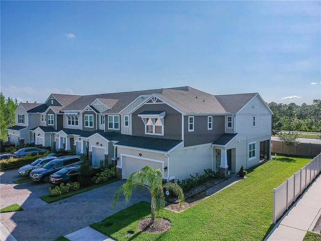 An exterior view of a multi-unit townhouse building with attached garages and a grassy yard — 18814 CORNUTA STREET, LUTZ, FL