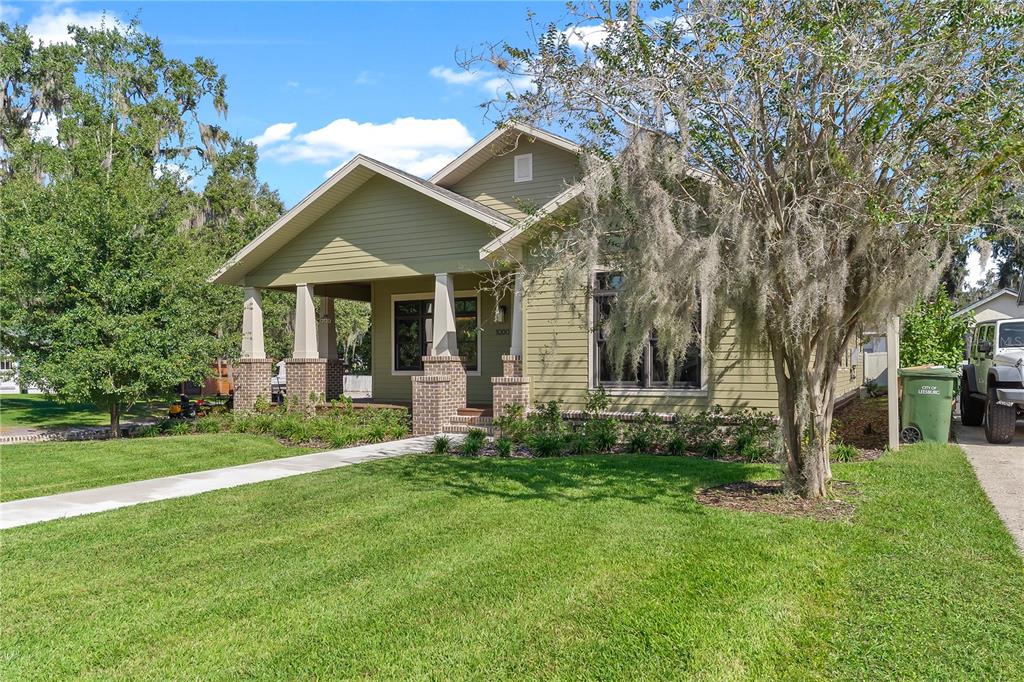 A green house with a covered front porch, brick columns, and a concrete walkway — 1000 S 9TH STREET, LEESBURG, FL