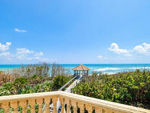 A balcony with a stone railing overlooks a wooden walkway leading to a beach gazebo — 8327 S Hwy A1a, Melbourne Beach FL 32951, MELBOURNE BEACH, FL
