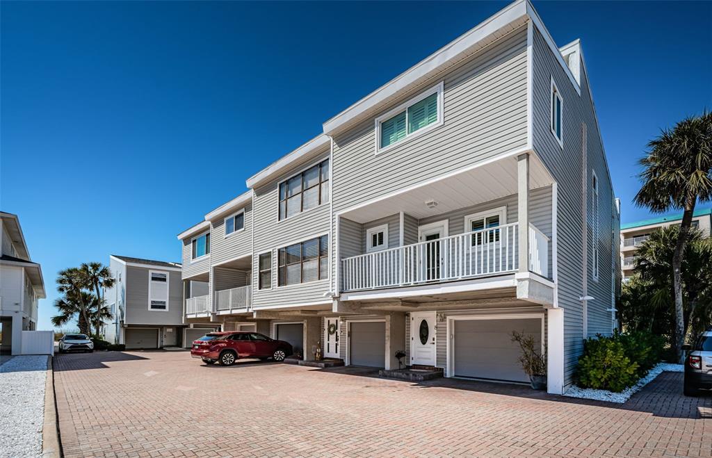 A multi-story townhouse with gray siding, a brick driveway, and multiple garage doors — 12274 1ST STREET W UNIT 8, TREASURE ISLAND, FL