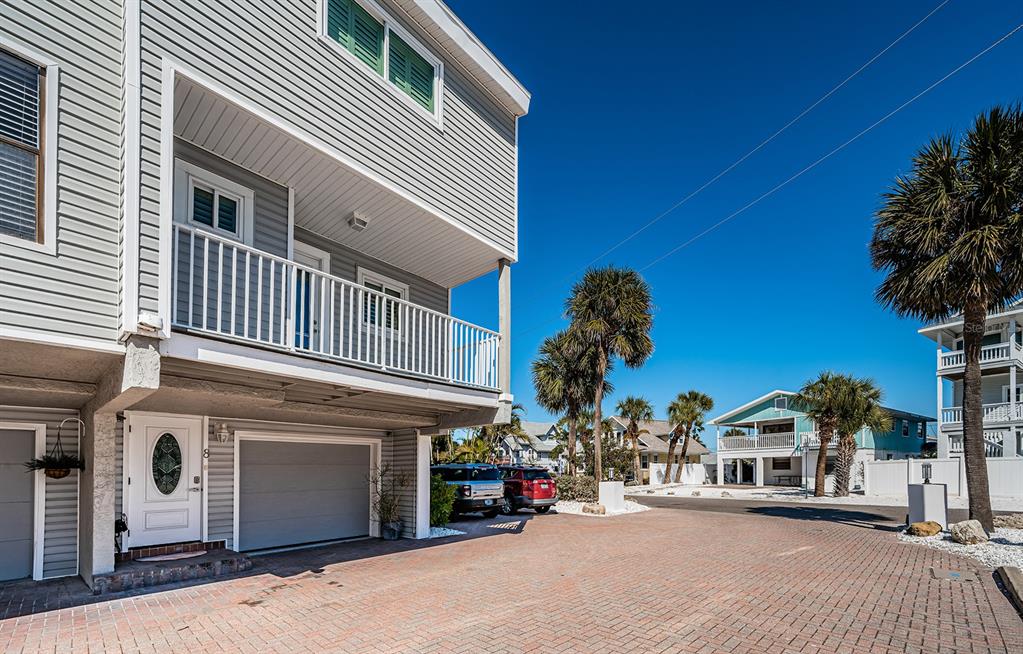 A multi-story gray house with a balcony, garage, and brick driveway under a clear sky — 12274 1ST STREET W UNIT 8, TREASURE ISLAND, FL