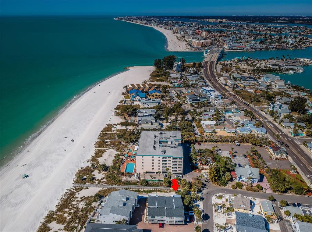 An aerial view shows a beachfront condominium complex and nearby houses along a sandy coast — 12274 1ST STREET W UNIT 8, TREASURE ISLAND, FL