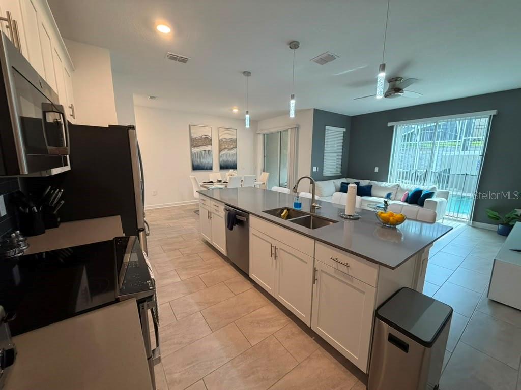 A modern kitchen with white cabinets and a large island overlooks an open living area — 1172 KINGSBARN STREET, DAVENPORT, FL