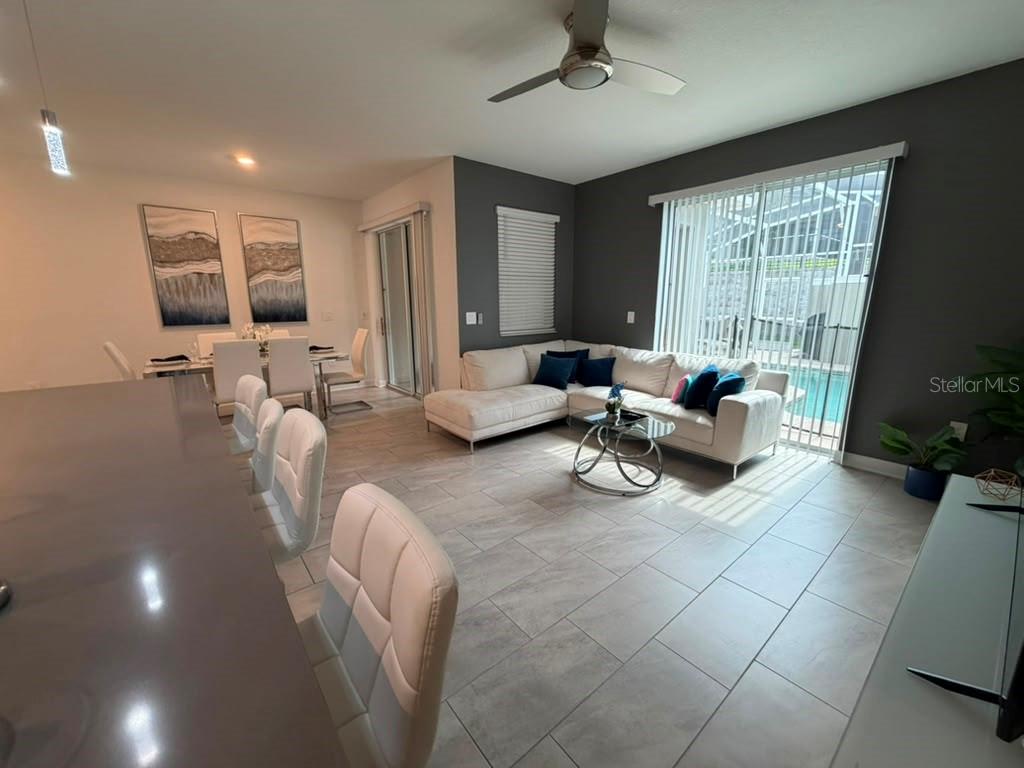 An open-concept living and dining area features tile floors, a sectional sofa, and pool views — 1172 KINGSBARN STREET, DAVENPORT, FL