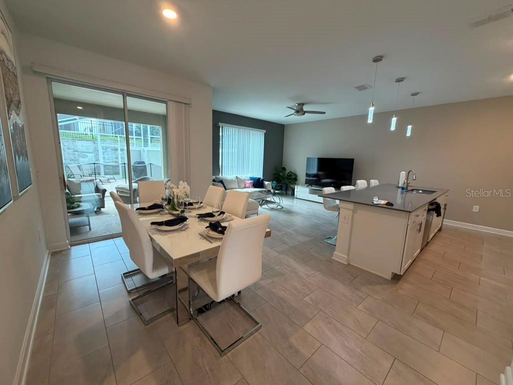An open-concept dining area and kitchen feature tile flooring, white furniture, and a sliding door — 1172 KINGSBARN STREET, DAVENPORT, FL