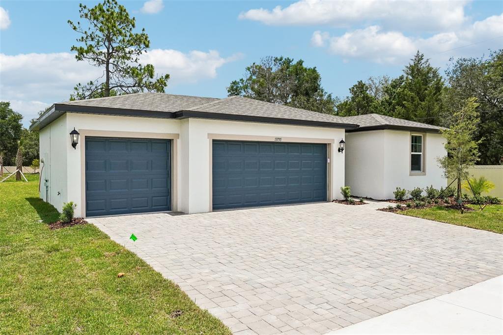 A single-story house exterior features a three-car garage, white stucco walls, and a paved driveway — 13755 UMBER FOREST STREET, HUDSON, FL