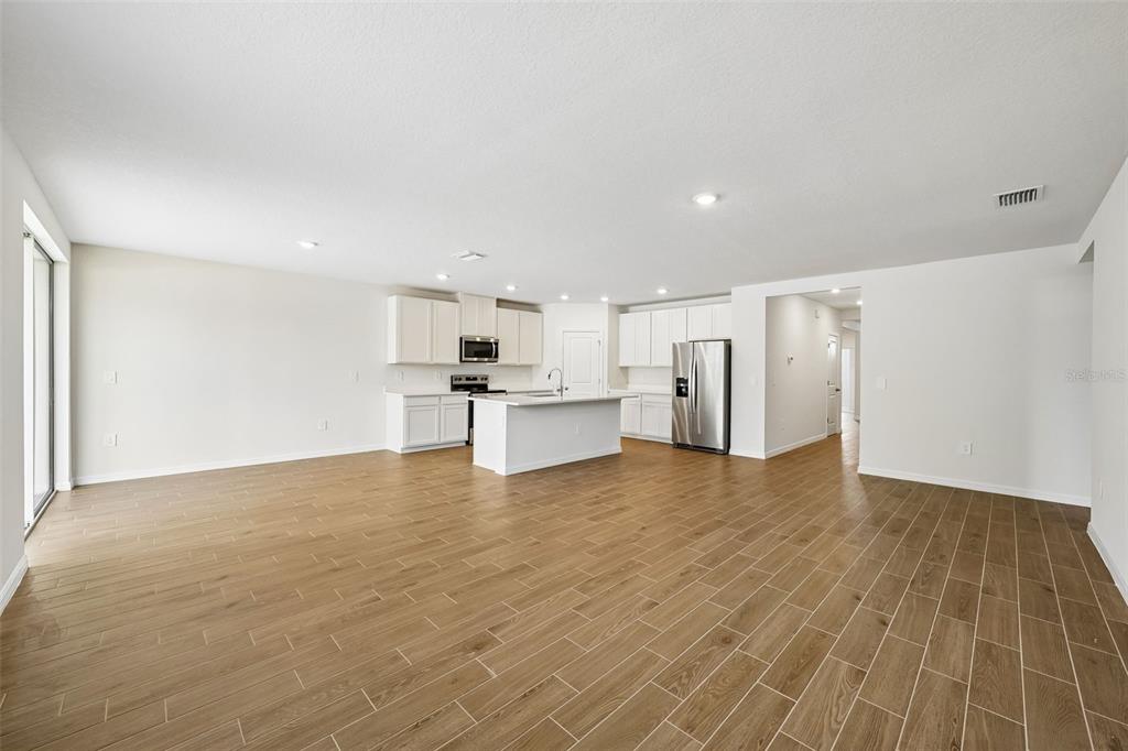 An open-concept kitchen and living area featuring white cabinets, stainless steel appliances, and wood-look flooring — 13755 UMBER FOREST STREET, HUDSON, FL