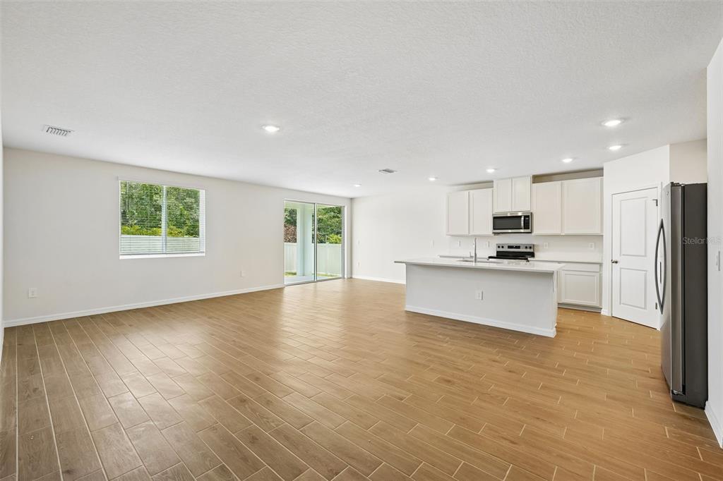 An open-concept kitchen and living area featuring light wood-look tile flooring and white cabinetry — 13755 UMBER FOREST STREET, HUDSON, FL