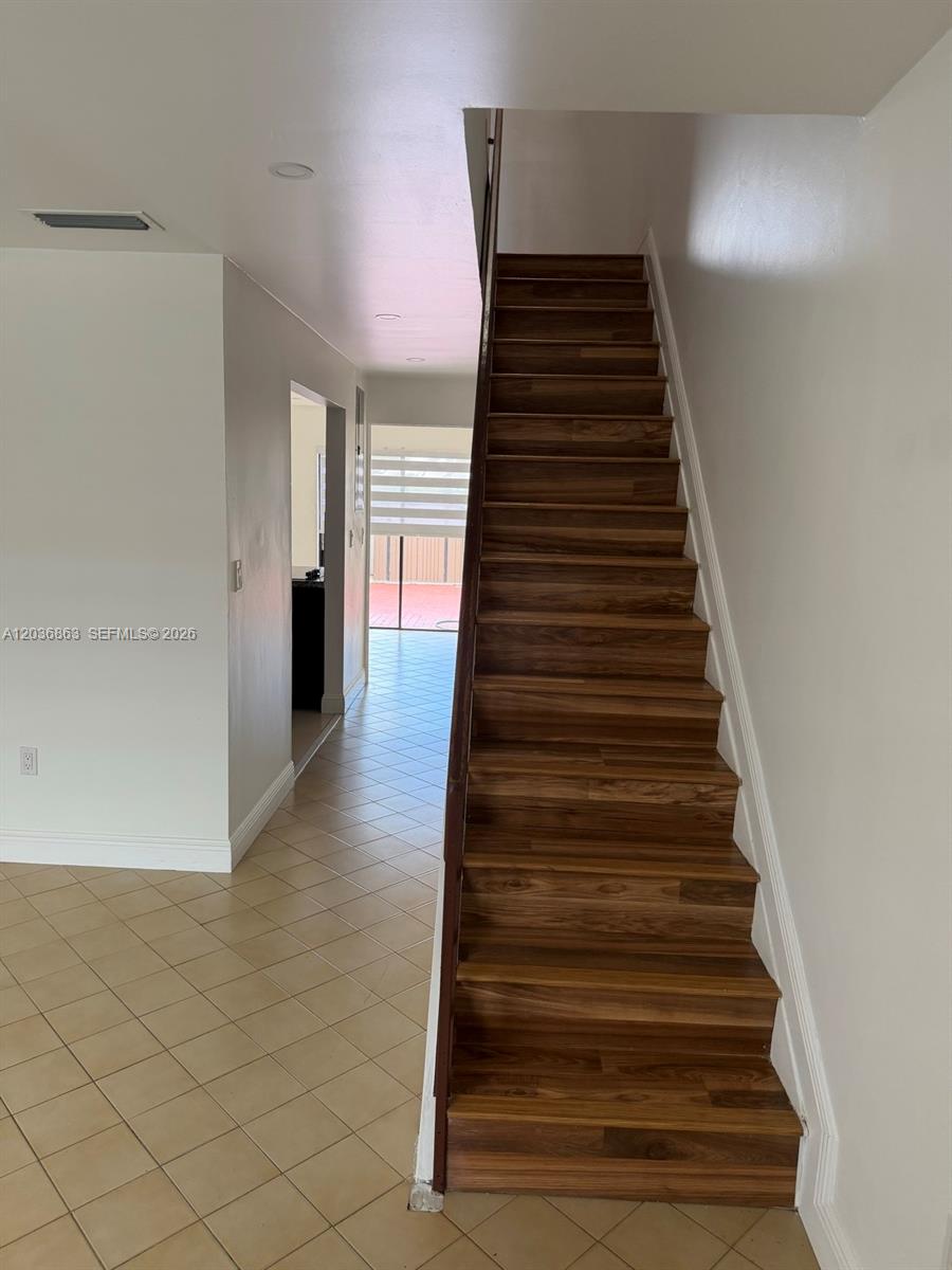 A staircase with wood-look treads ascends alongside a tiled floor in a residential interior — 13335 SW 57th Ter # 3, Miami FL 33183, MIAMI, FL