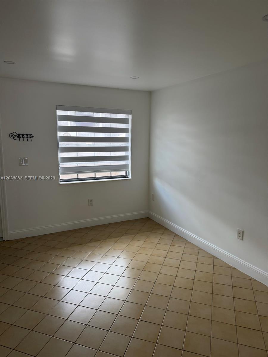 An empty room features white walls, tan tile flooring, and a window with zebra blinds — 13335 SW 57th Ter # 3, Miami FL 33183, MIAMI, FL