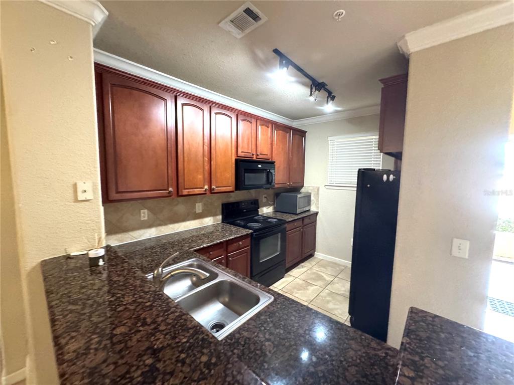 A kitchen features dark wood cabinets, granite countertops, black appliances, and a double-basin sink — 909 CHARO PARKWAY UNIT 1016, DAVENPORT, FL