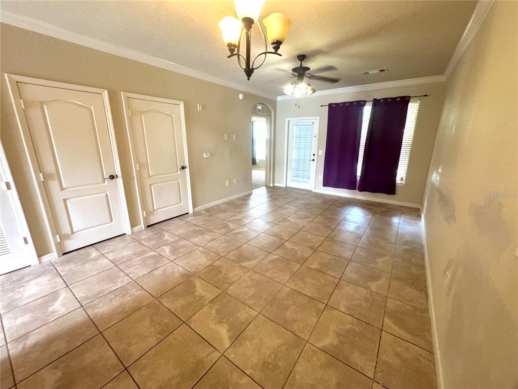 An empty room features tan tile flooring, beige walls, a ceiling fan, and purple curtains — 909 CHARO PARKWAY UNIT 1016, DAVENPORT, FL